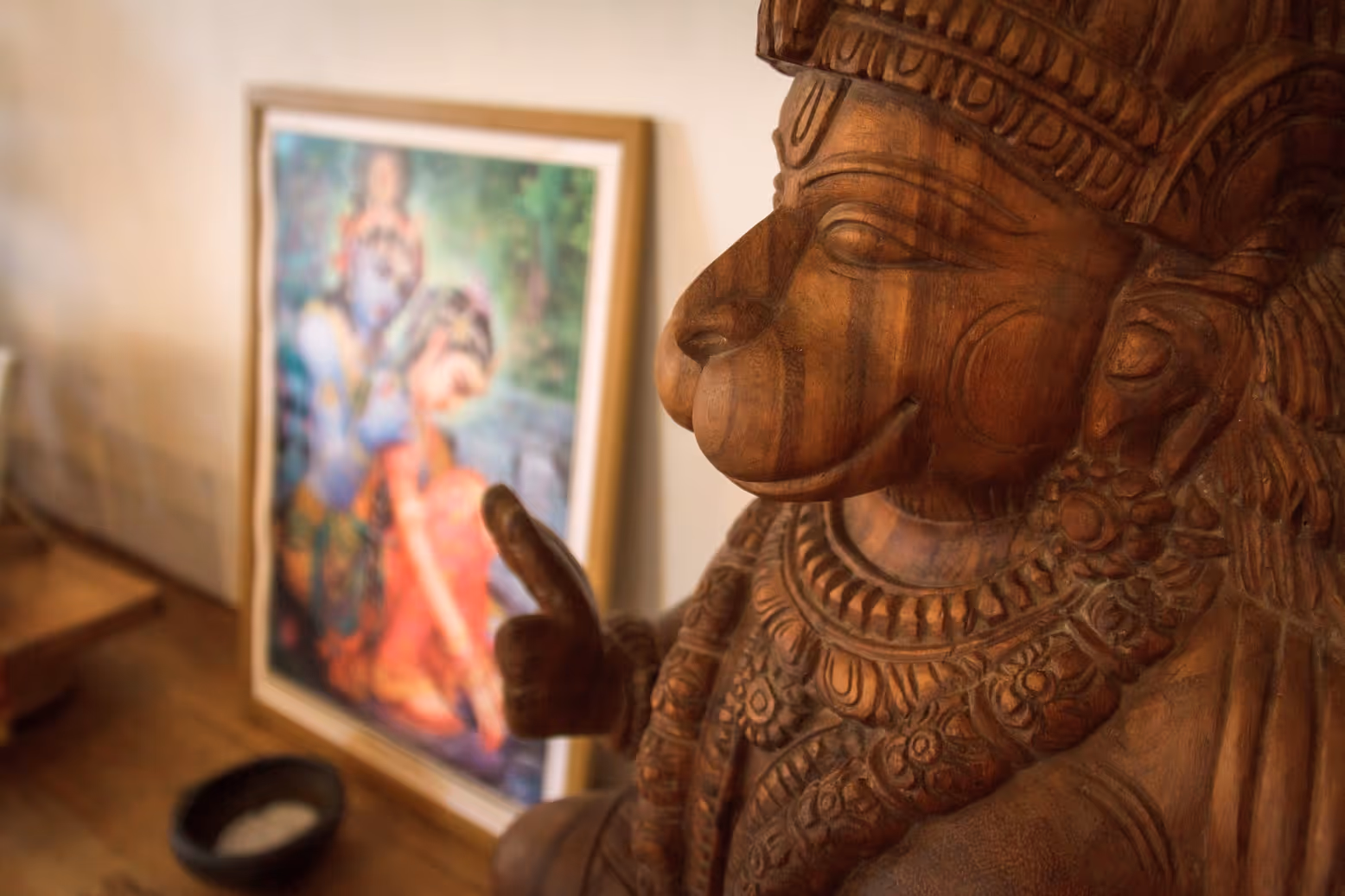 Wooden sculpture of Hanuman with a painting of Radha Krishna in the background
